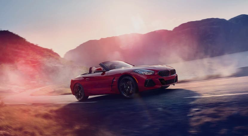 A red 2021 BMW Sports car, a Z4, is driving on road past mountains and a lake.