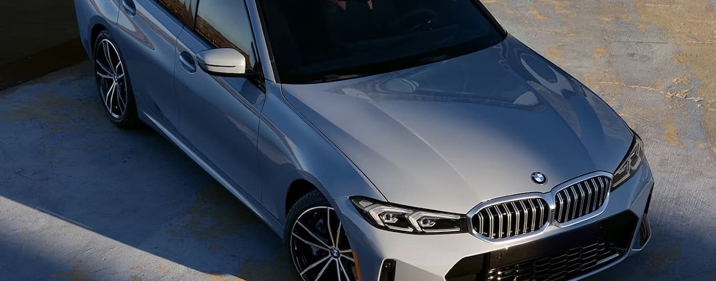 A grey 2024 BMW 3 Series is shown parked in an open parking lot.