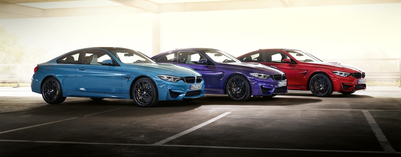 A blue, a purple, and a red 2020 BMW M4 coupe Edition M are shown from the side parked in an empty parking garage.