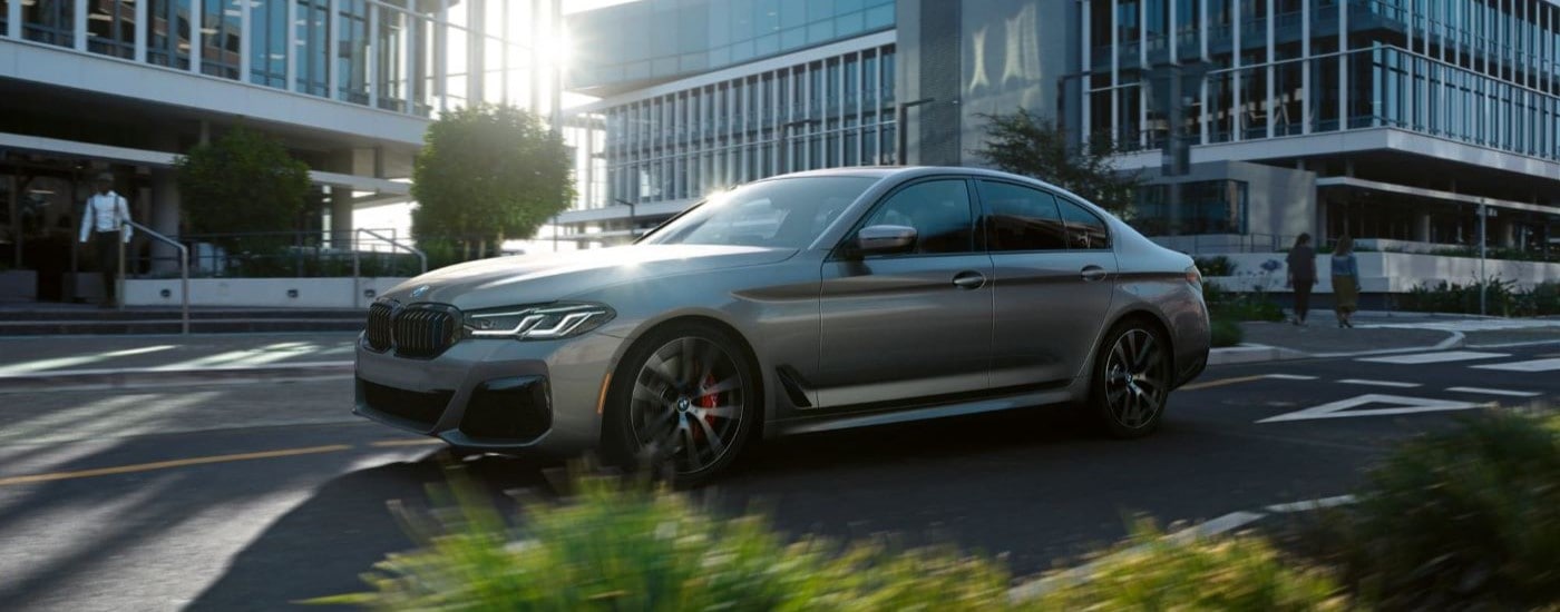 A silver 2023 BMW 5 Series for sale is shown on a city street.