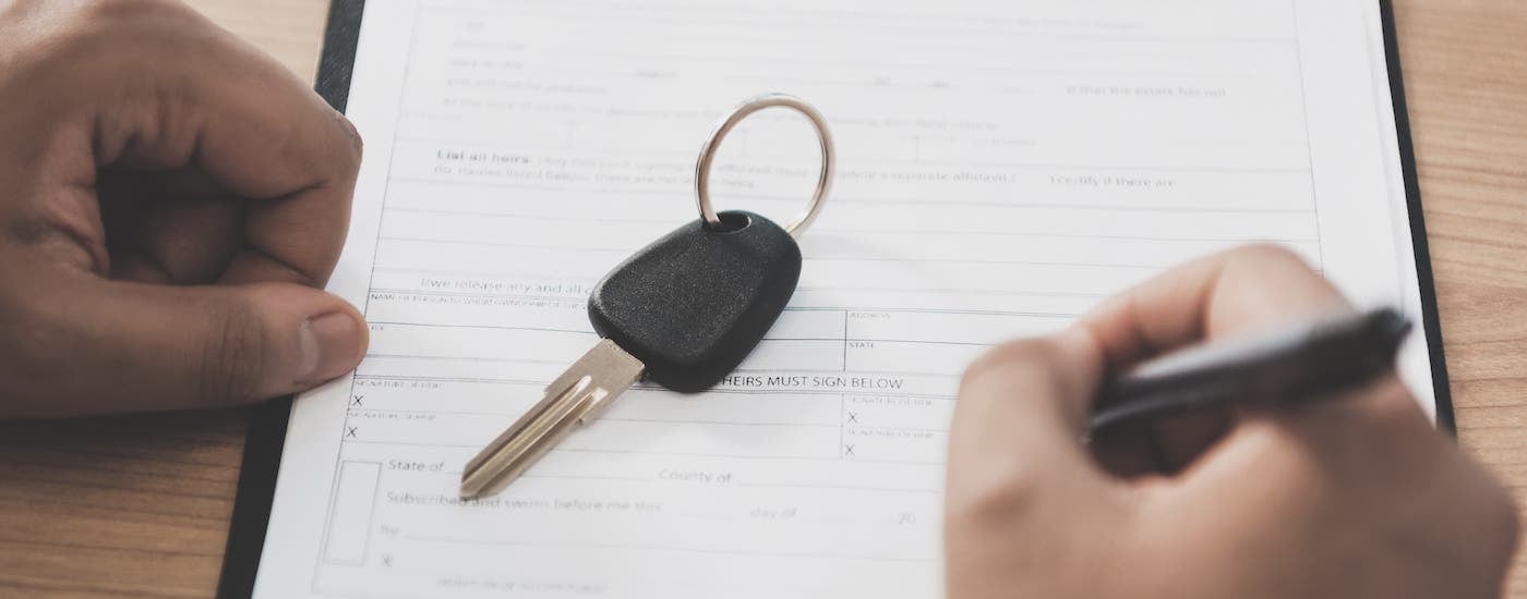 A closeup shows hands and a car key on a BMW lease deal agreement.