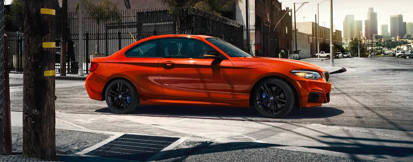 An orange 2020 BMW 2 Series Coupe is driving on a city street after someone searched for a used BMW near them.