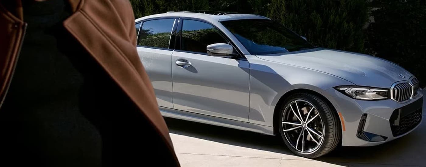 A silver 2024 BMW 3 Series is shown parked on the side of a city street.