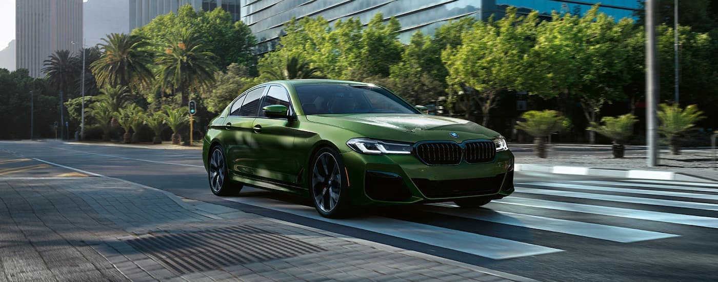 A green 2022 BMW M550i is shown driving through a city intersection.