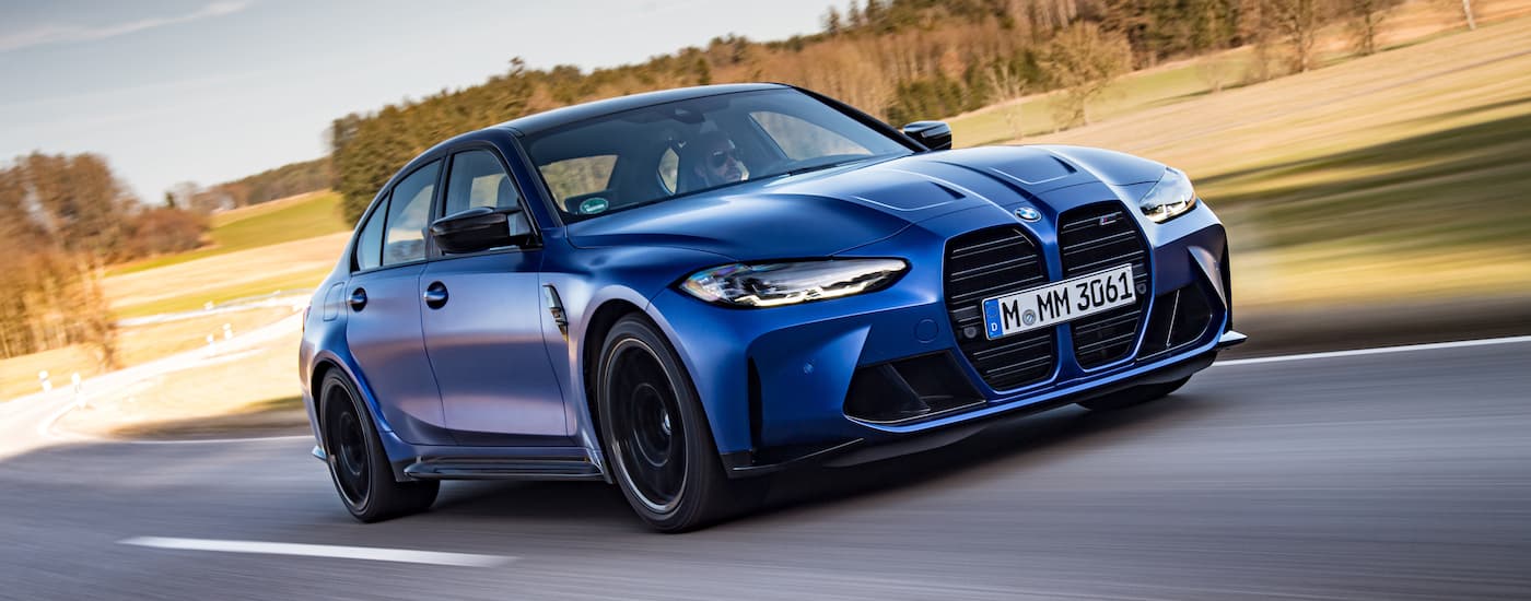 A blue 2022 BMW M3 Competition is shown driving on a open road.