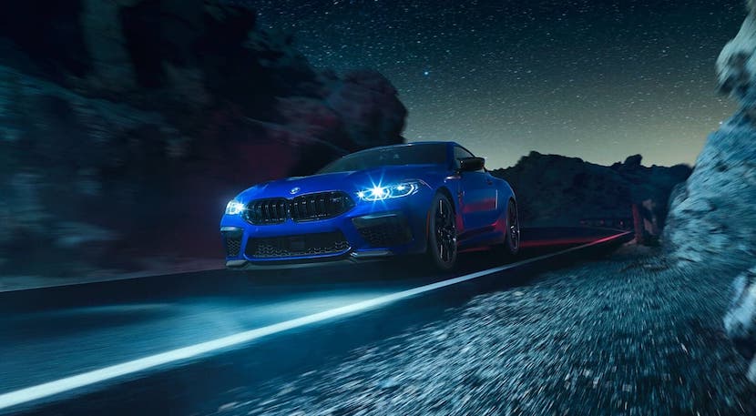 A blue 2021 BMW M8 coupe is driving on a highway at night.