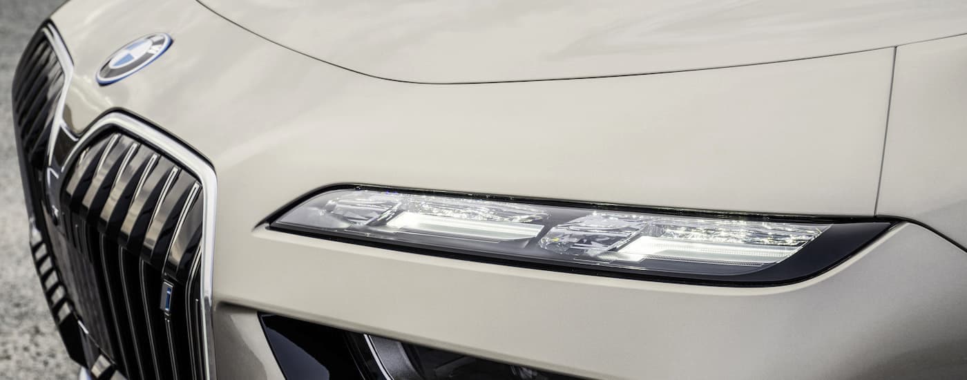 A close up shows the driver side headlight on a tan 2022 BMW i7.