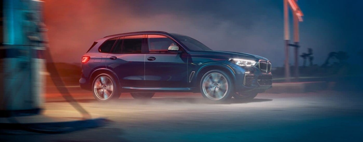 A blue 2020 BMW X5 for sale is shown from the side driving at night.