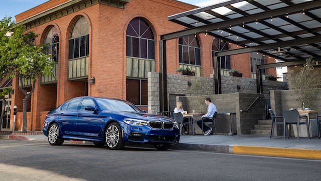A blue 2020 BMW 5 Series 530e is parked in front of a cafe in Cincinnati.