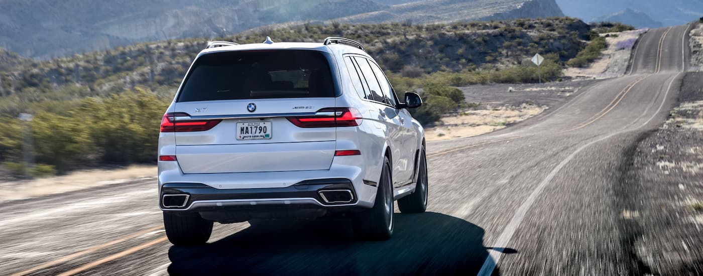 A white 2021 BMW X7 is shown from the rear driving on a hilly road.