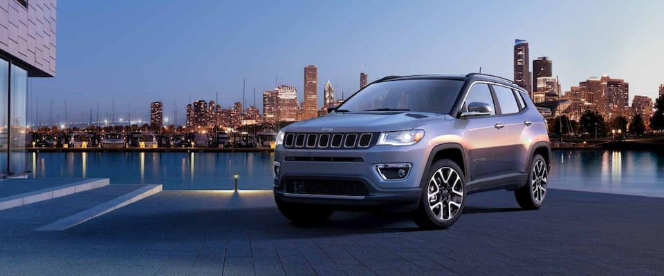 A silver 2019 Jeep Compass parked in front of a city skyline