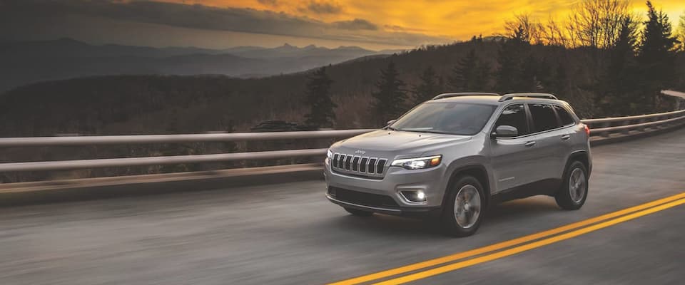 A silver 2019 Jeep Cherokee driving down the road at sunset