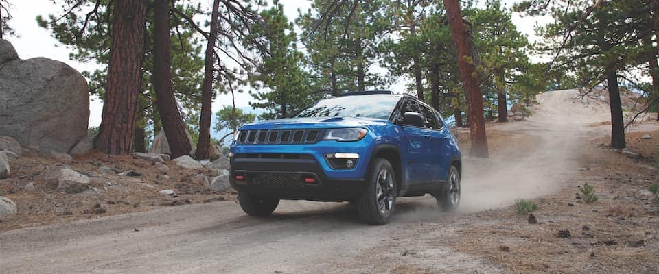 A blue Jeep Compass driving on a dirt path