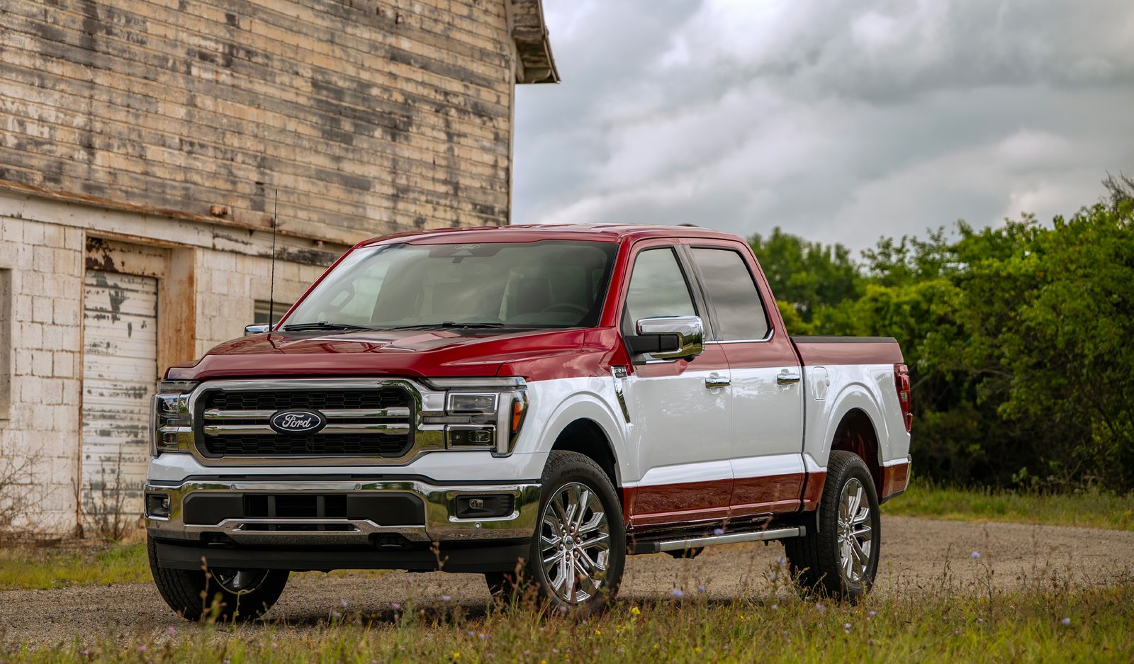 2027 Ford F-150 Lariat SuperCrew in Ruby Red with the Ford Custom Garage Custom Two-Tone Oxford White paint stripe, parked in front of an old barn