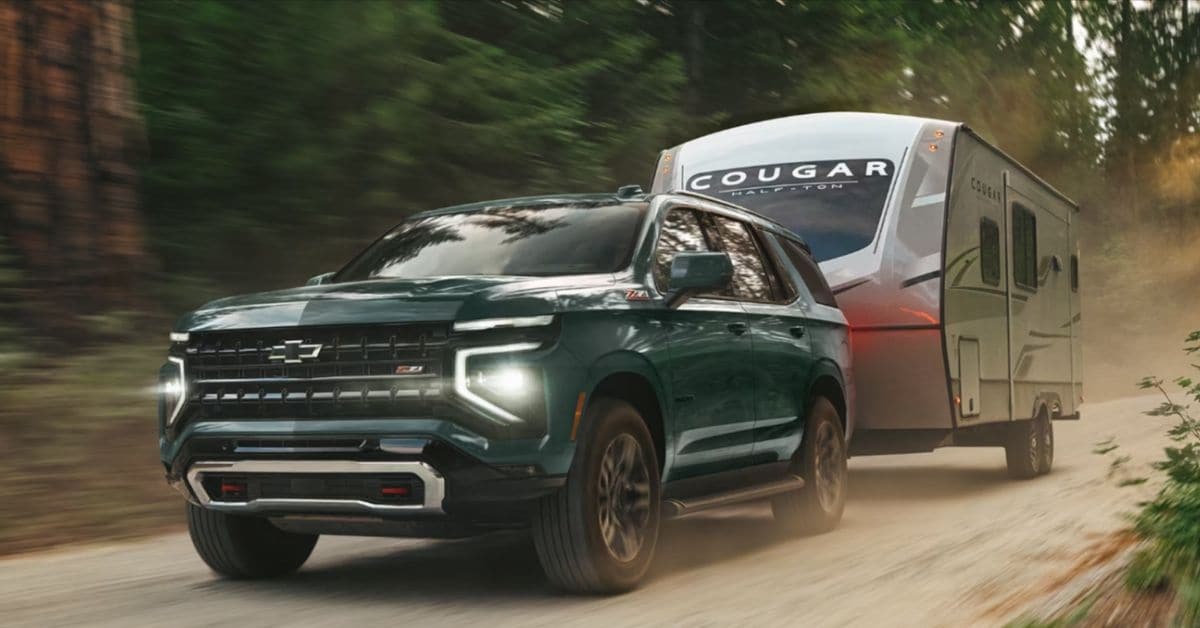 Green 2026 Chevrolet Tahoe Z71 towing a Cougar Half-Ton travel trailer on a dusty forest road.