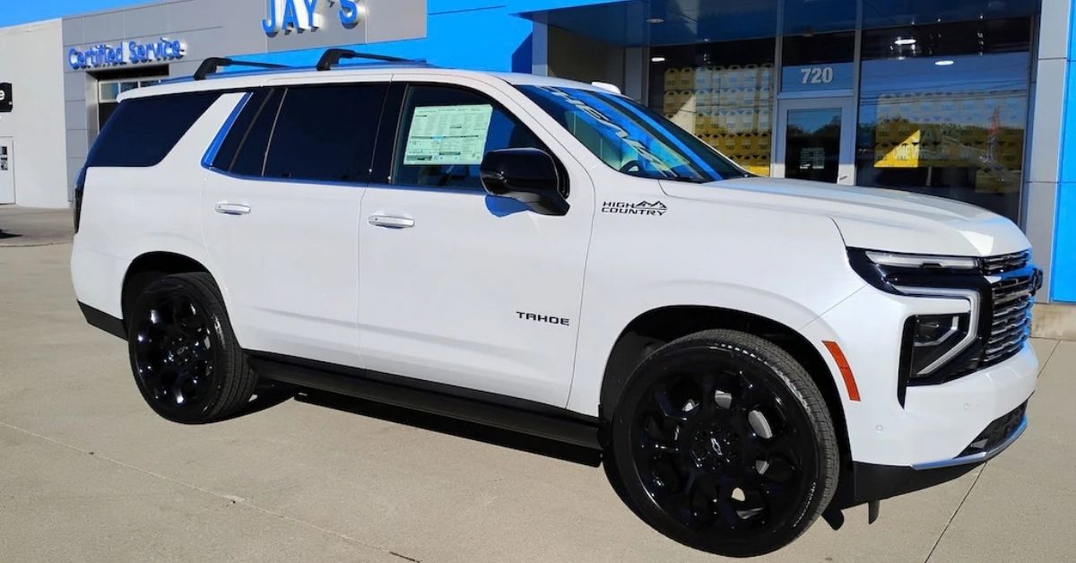 White 2026 Chevrolet Tahoe High Country SUV with black wheels and tinted windows parked on a concrete lot in front of Jay’s Chevrolet GMC dealership building in daylight.