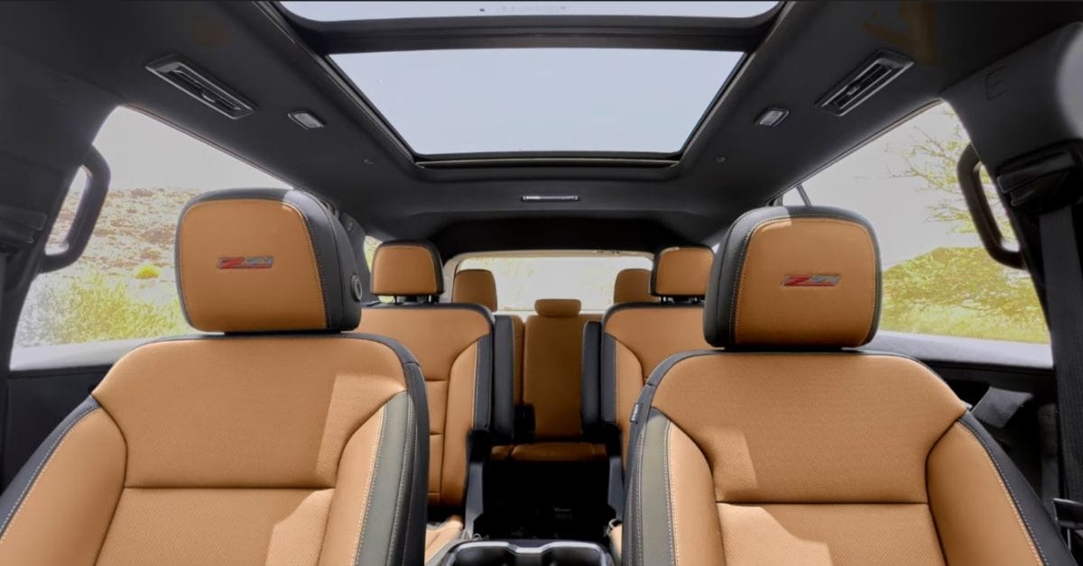 Wide view of a 2027 Chevrolet Traverse Z71 three-row SUV interior featuring tan and black leather seats, embroidered Z71 headrests, second-row captain’s chairs, and a large panoramic sunroof.