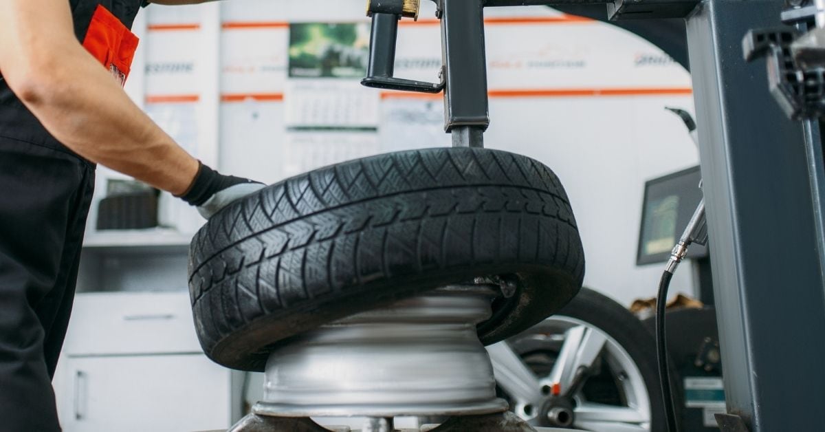 Technician mounting a vehicle tire on a professional tire-changing machine in an auto service shop.