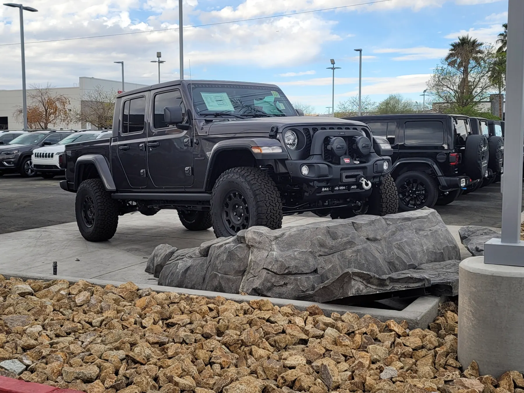 Lifted gray Jeep Gladiator with off-road bumper lighting parked beside the rock display at the Jeep Only entrance in Las Vegas