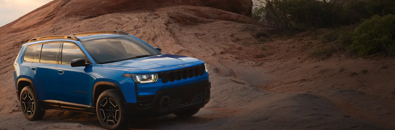 Blue Jeep Cherokee Trailhawk on red rock at sunset, a build Las Vegas shoppers can custom order