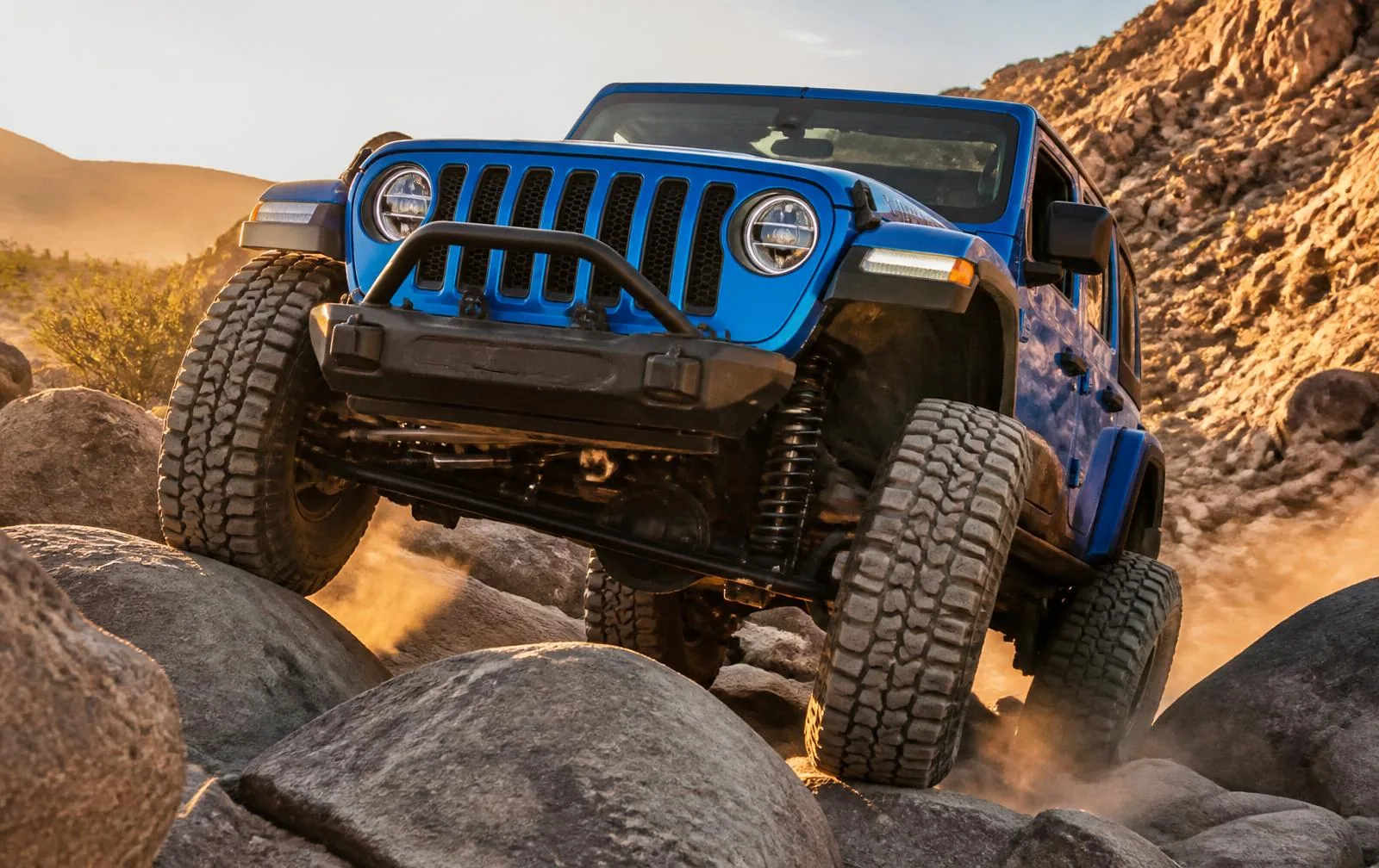 Blue Jeep Wrangler rock crawling on rugged desert terrain for a Wrangler vs Ford Bronco comparison