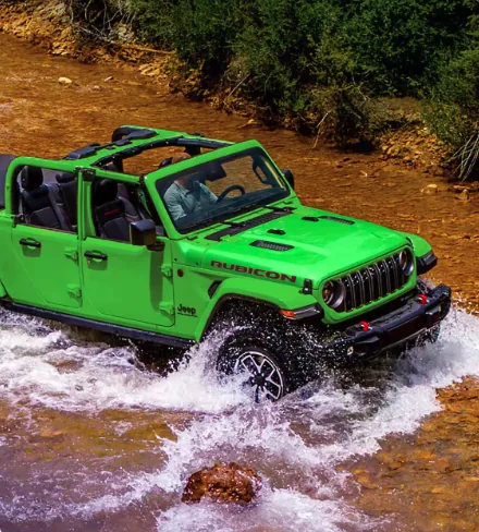 Bright green Jeep Wrangler Rubicon crossing a shallow stream off road
