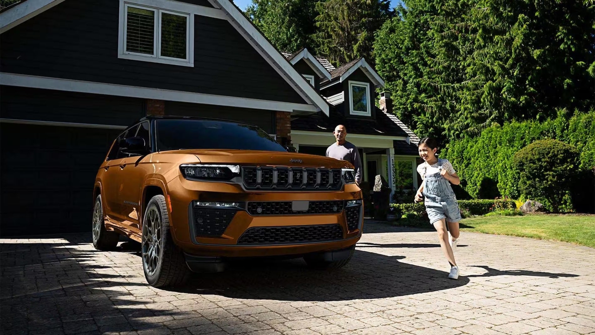 Copper 2027 Jeep Grand Cherokee parked in a home driveway, front three-quarter view