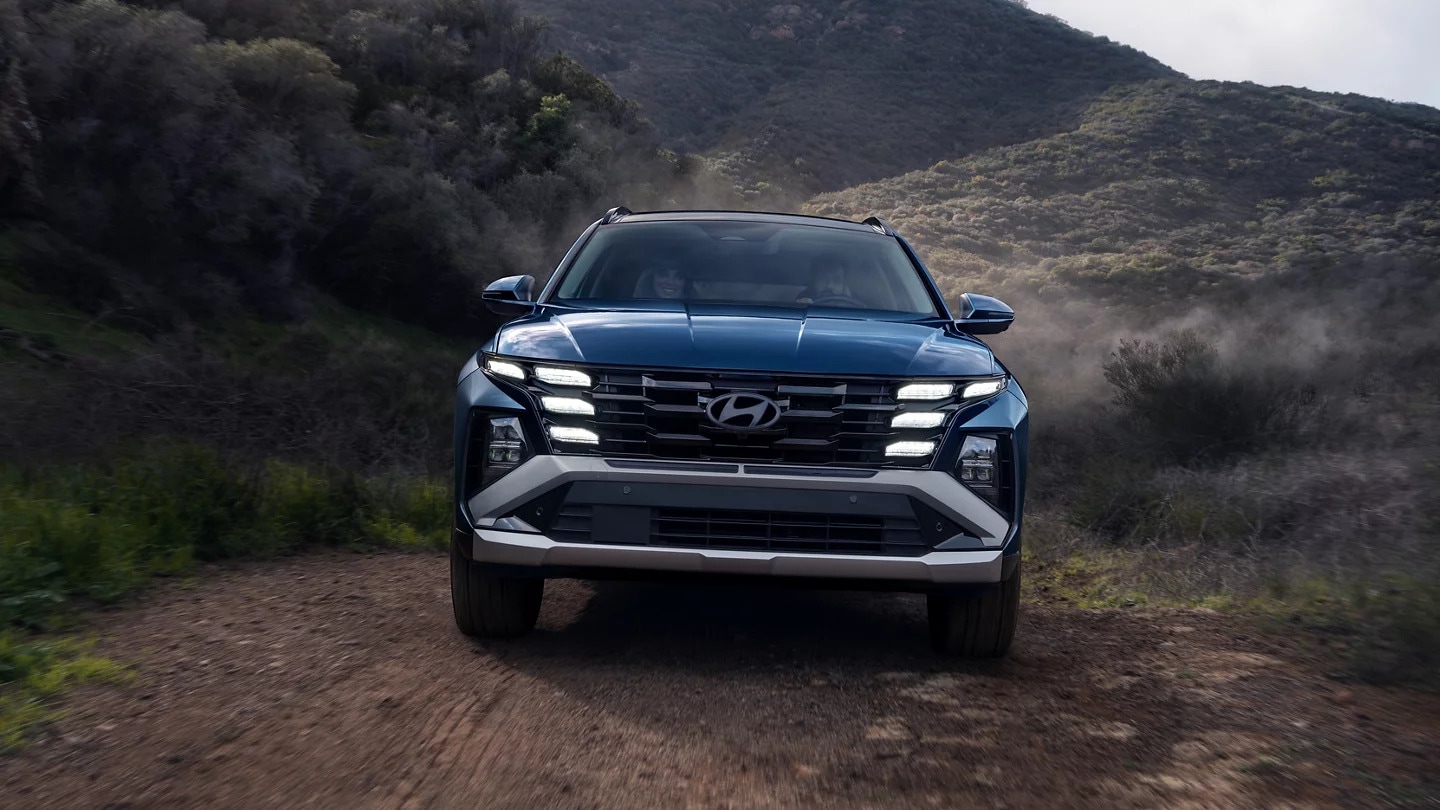 A front view of a blue Hyundai Tucson driving on a dirt road