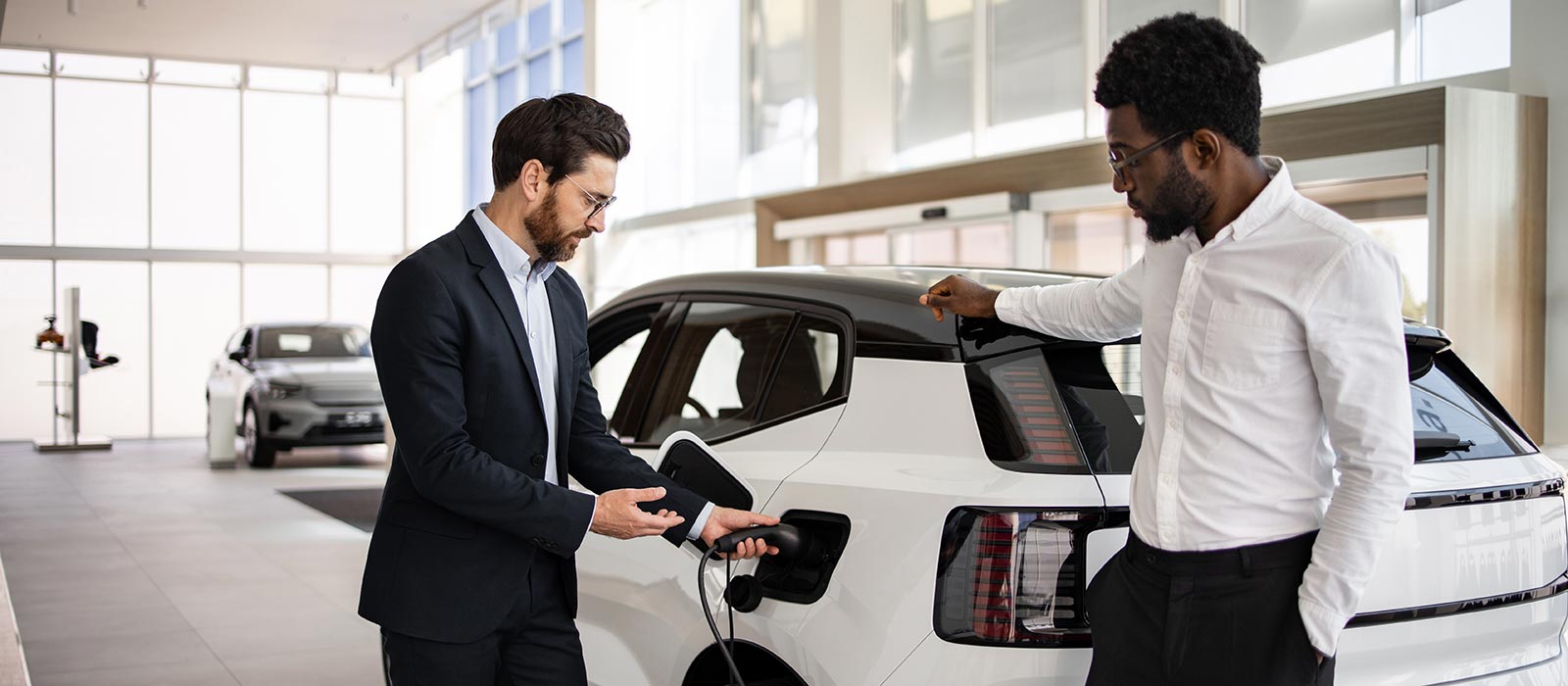 A car salesman showing off a plug-in electric vehicle to a customer.