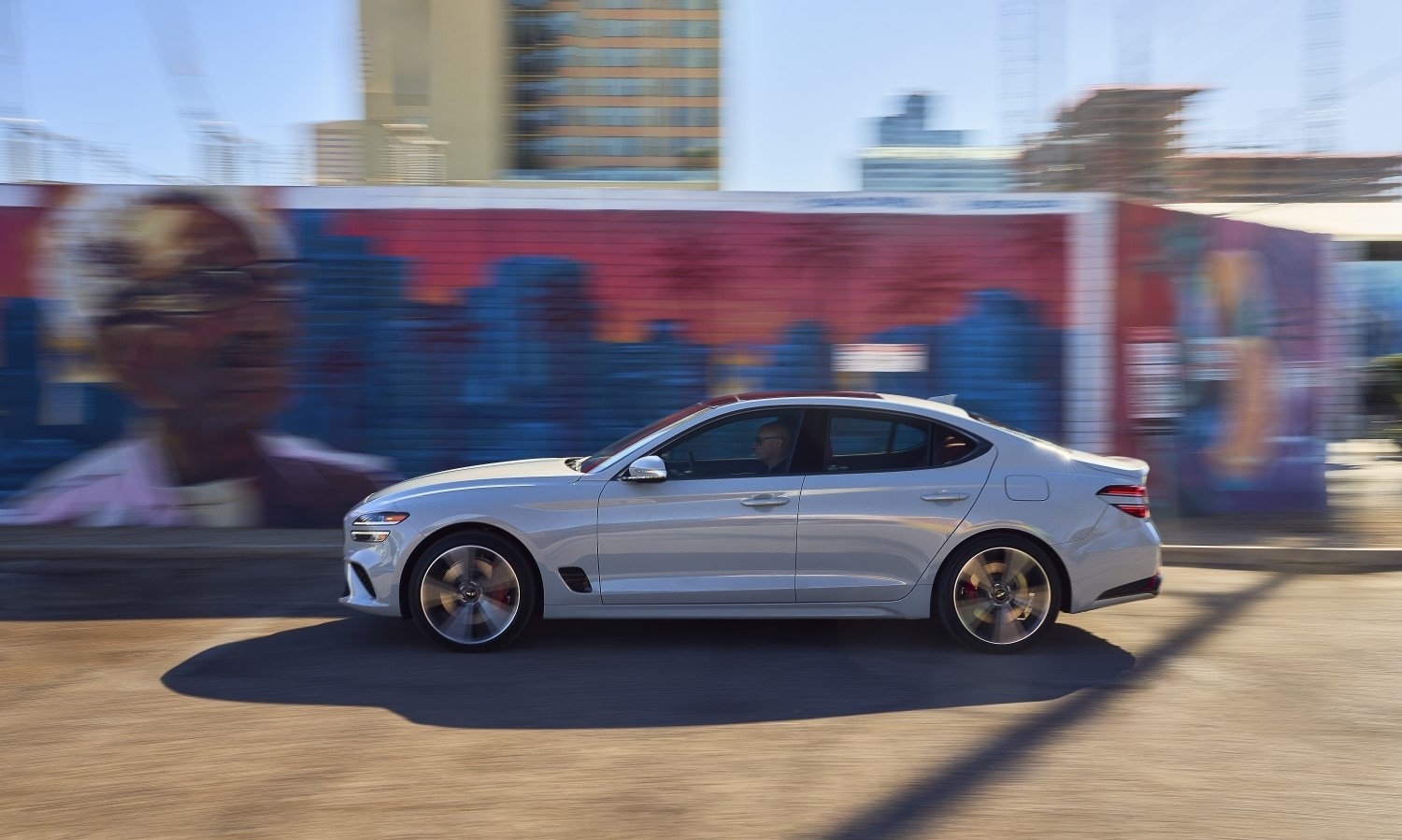 Genesis G70 sedan in white, cruising past a mural