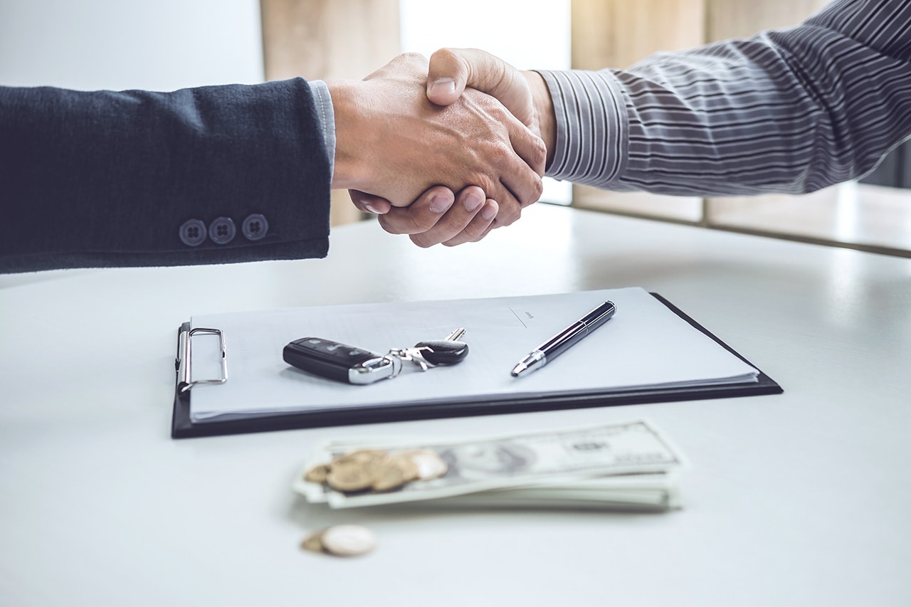 Two people shaking hands over vehicle paperwork
