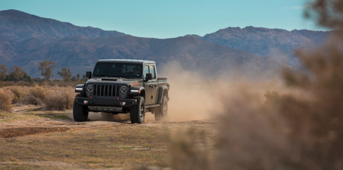black Jeep Gladiator truck kicking up dust on a desert road