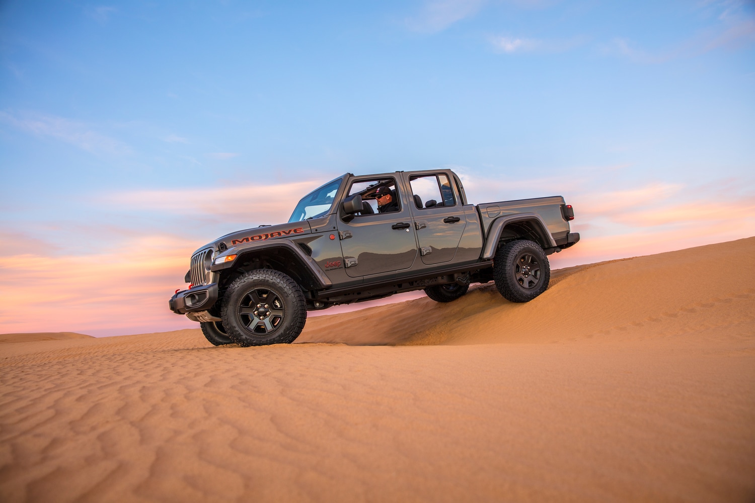 dark gray Jeep Gladiator truck driving down a sandy desert hill