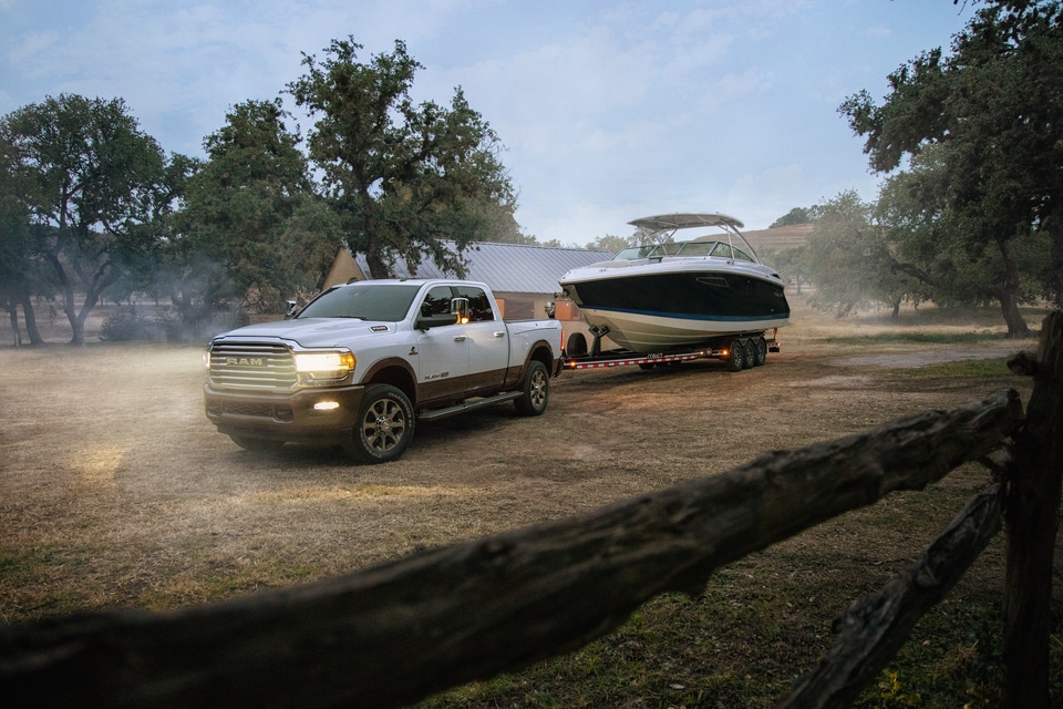 white Ram 2500 truck towing a boat with headlights on