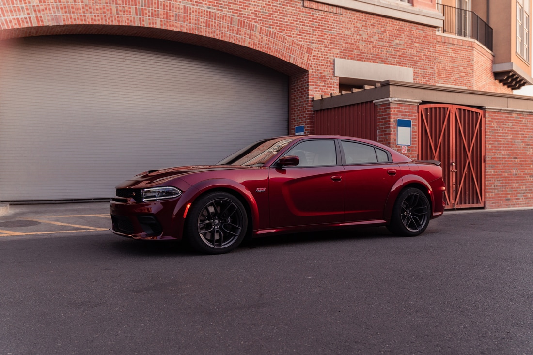 dark red Dodge Charger sedan parked in front of a brick-lined garage door