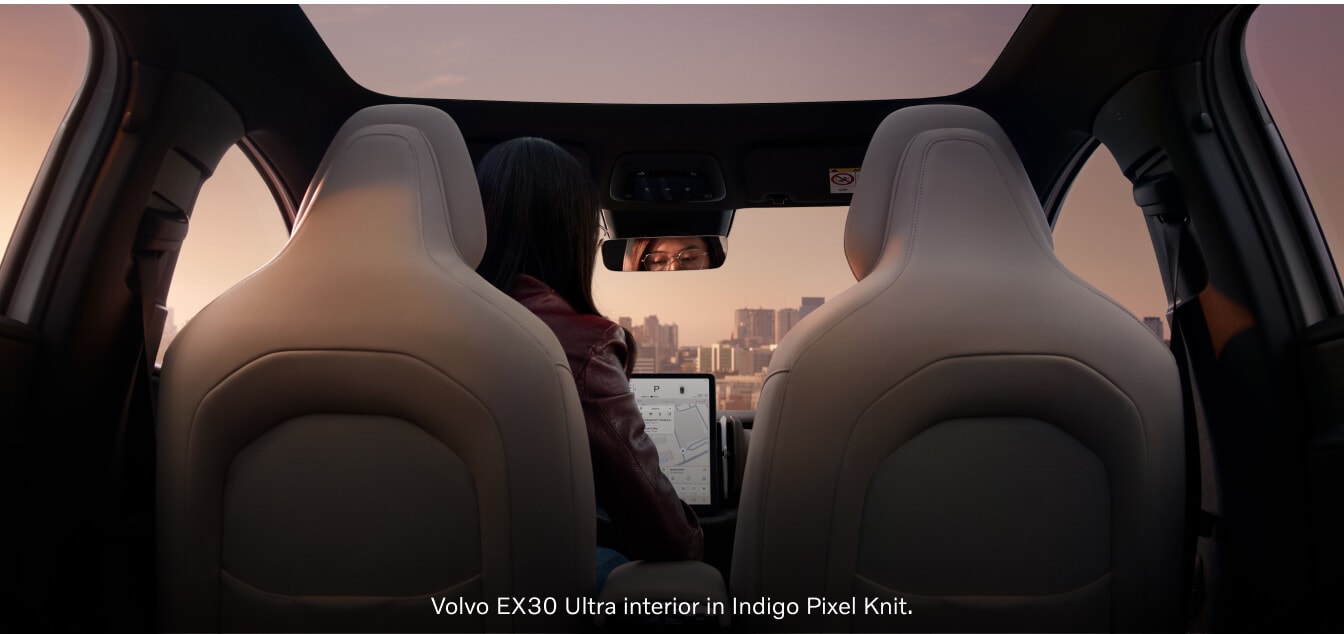 Rear-seat perspective view of a Volvo EX30 cabin a panoramic glass roof at sunset.