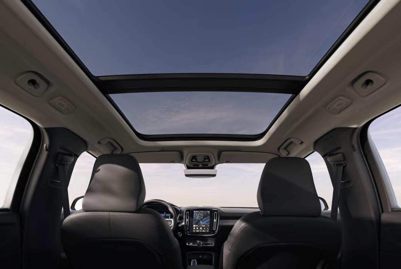 View from the backseat of a 2026 Volvo XC40 showing a wide glass sunroof and front seats. The sky is visible, creating an open and airy atmosphere.