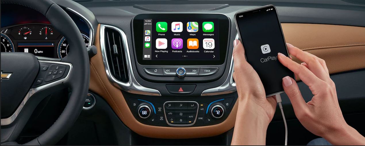 Centered: Woman activates Apple CarPlay from the passenger seat. The CarPlay user interface appears on the eight inch touch screen control panel.