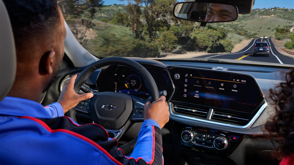 Driver holding the steering wheel of a Chevrolet vehicle with navigation displayed on the infotainment screen.