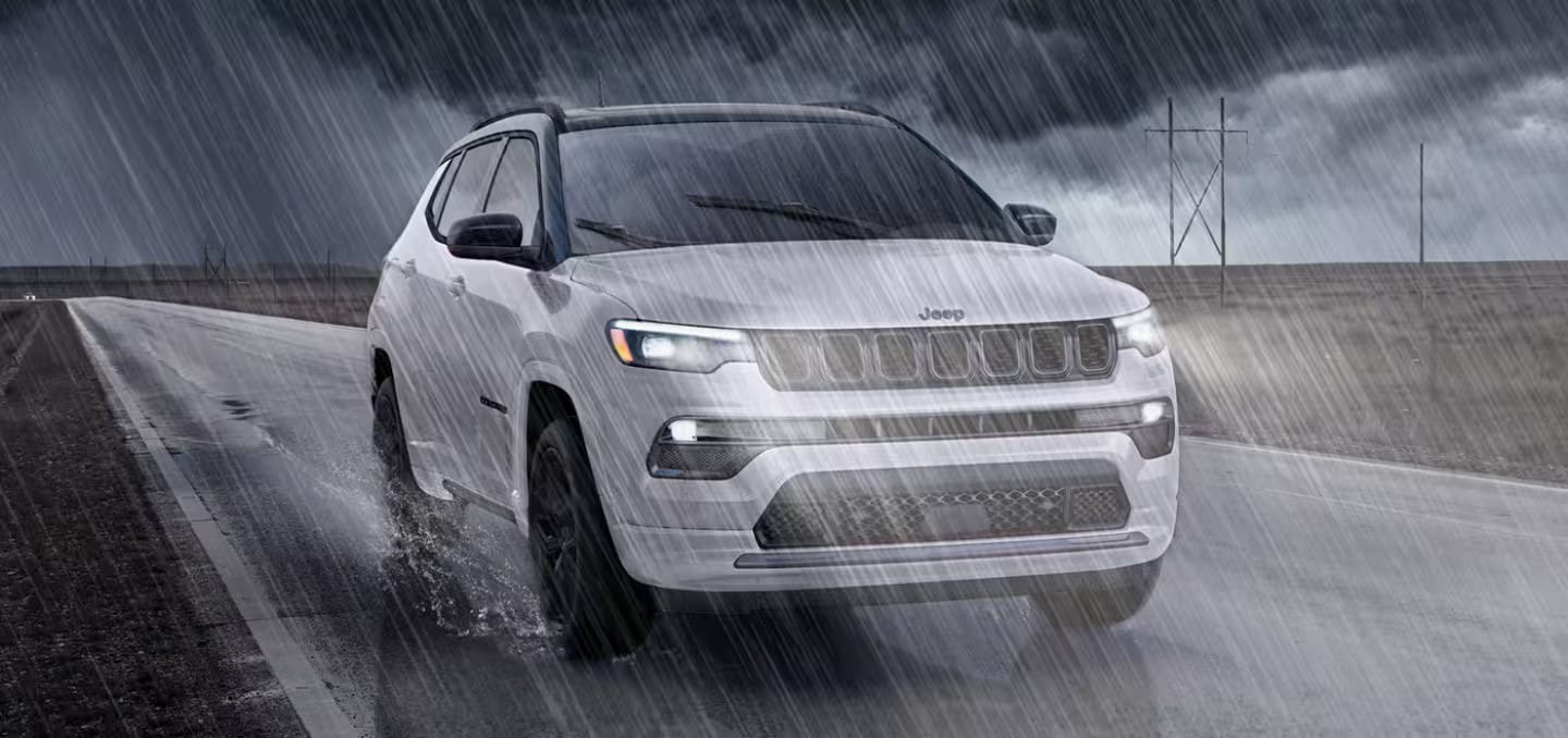 A white jeep driving on a road in the rain.