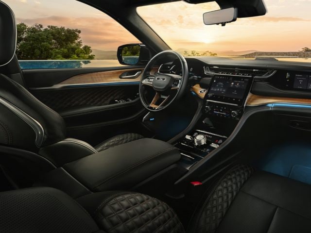 Interior photo of a 2022 Grand Cherokee showing luxury black leather seats, the instrument panel, steering wheel, and wood-paneled dashboard features