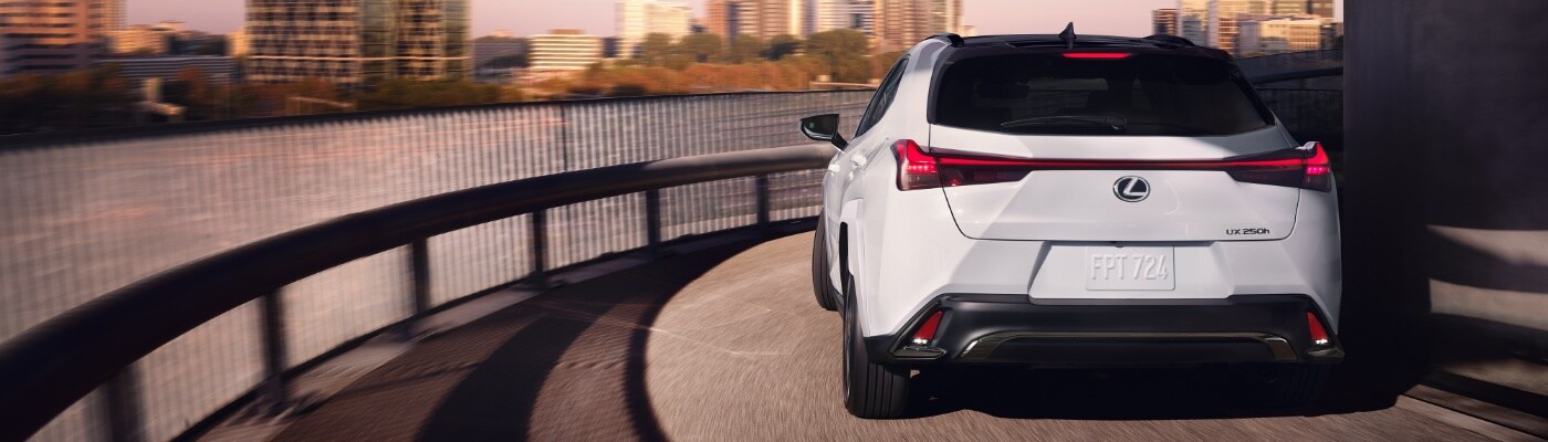 White Lexus UX 250h driving around a circular section of road overlooking water