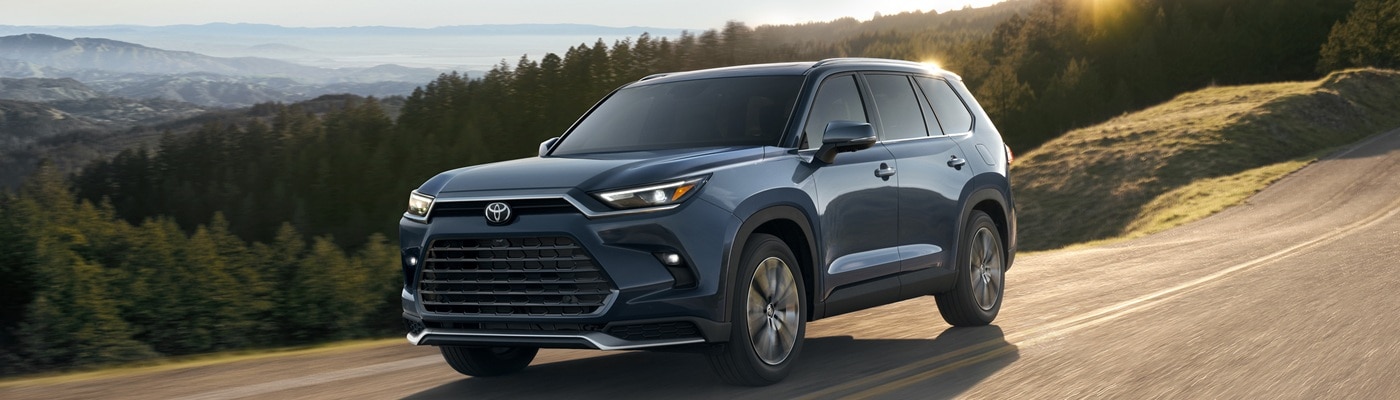 Blue Toyota Grand Highlander Hybrid driving on a road in the forest