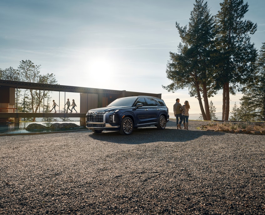 2023-Hyundai-Palisade-Calligraphy-SUV-L03.png dark blue Hyundai Palisade parked in the sand in front of a lake house