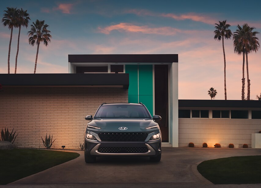 Hyundai-Kona-EV-SUV-L04.png grey Hyundai Kona EV parked in a driveway flanked by palm trees