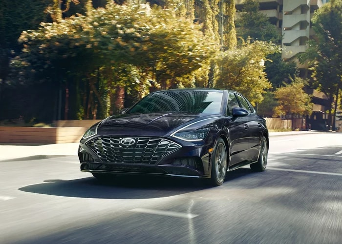 black Hyundai Sonata driving on a tree-lined city street