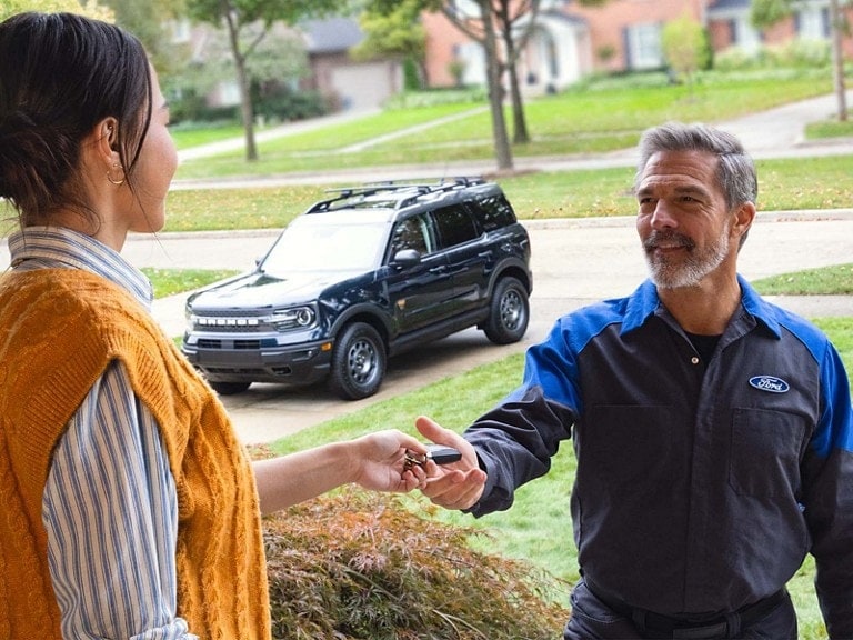 Ford service tech at a customer's home is handed their Bronco Sport keys to perform Pickup & Delivery service