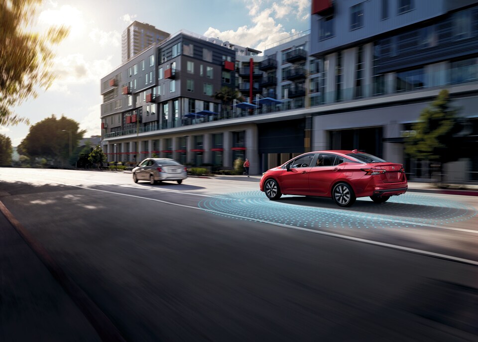 Red Nissan Versa driving down busy street with graphic illustrating Nissan's intelligent Collision system