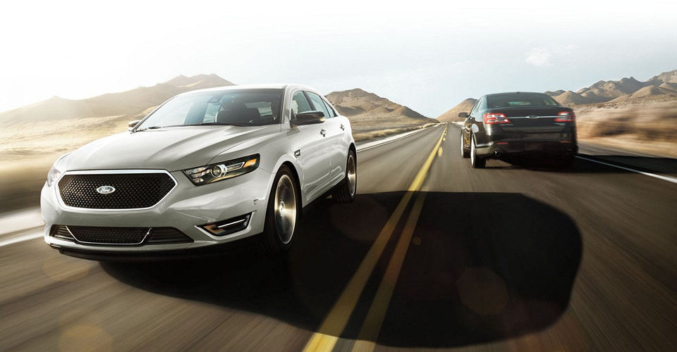 A silver 2017 Ford Taurus driving past a black sedan