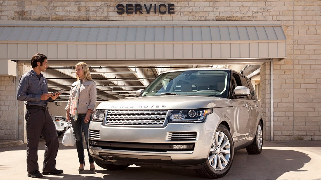 A silver Range Rover parked in front of a service center while a woman talks to a technician.